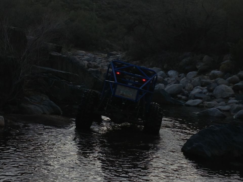 Blue off-road buggy with roll cage crossing shallow stream at dusk
