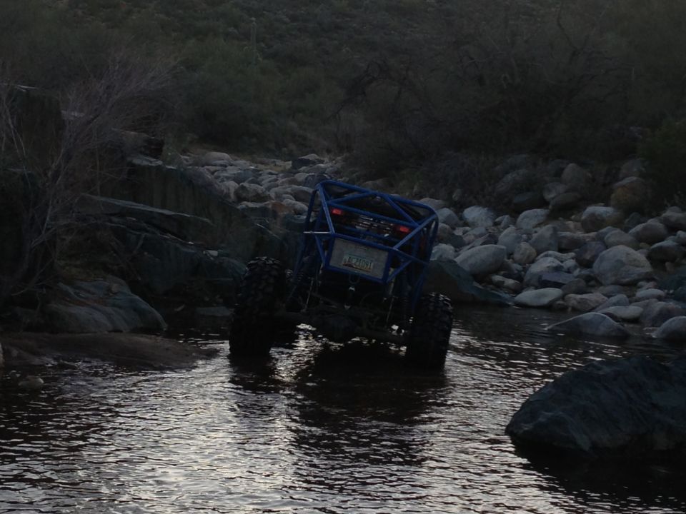 Blue off-road buggy driving through a rocky stream bed
