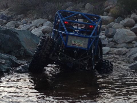 1966 Ford Bronco - A custom-built off-road buggy with a roll cage is shown driving through a rocky stream.
