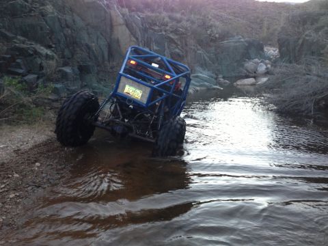 1966 Ford Bronco - Custom off-road buggy navigates through a rocky stream bed, its suspension and large tires.
