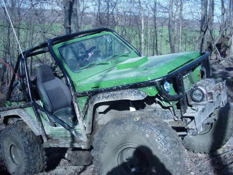 1992 Ford Bronco - A modified green off-road vehicle is seen in a wooded, muddy terrain.