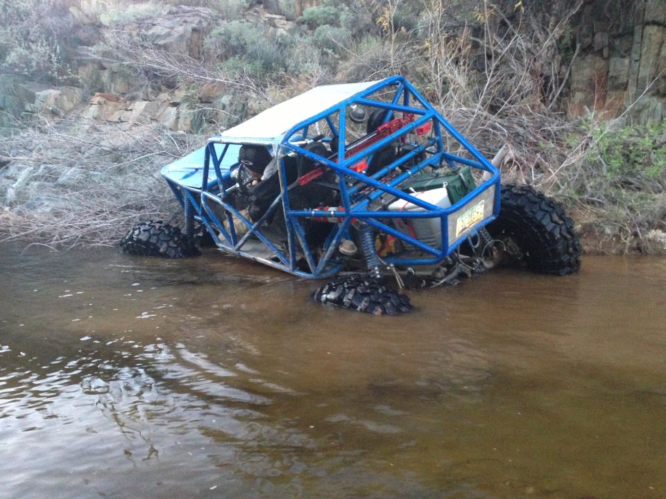 Blue off-road buggy with a roll cage, partially submerged in shallow water
