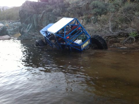 1966 Ford Bronco - An off-road buggy is partially submerged in a body of water next to a rocky embankment.