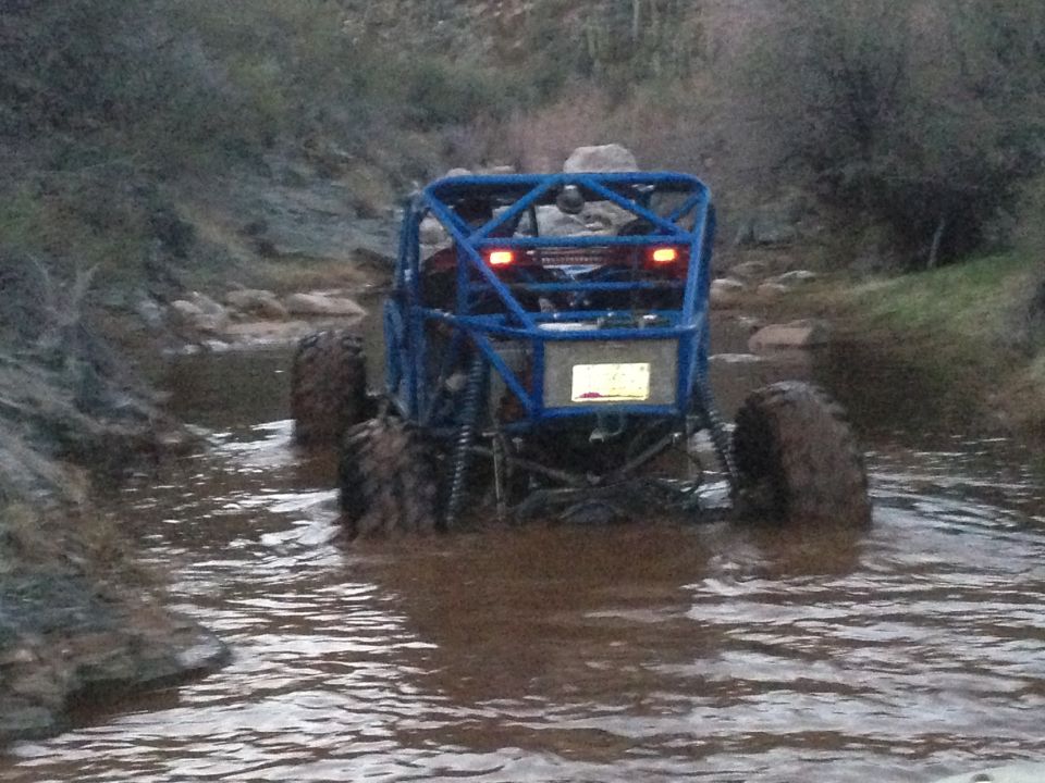 Blue off-road buggy with roll cage driving through muddy water