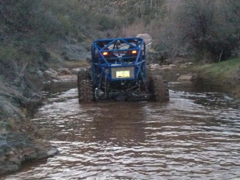 1966 Ford Bronco - A blue off-road buggy navigates a rocky stream bed, its large tires kicking up water.