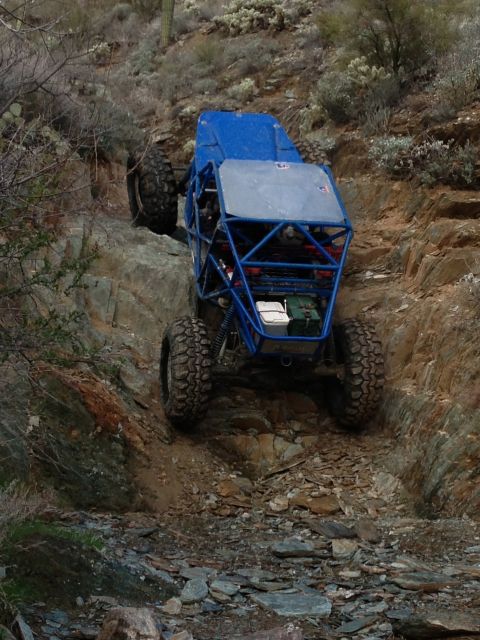 1966 Ford Bronco - A custom-built blue buggy navigates a steep, rocky trail in a desert environment.