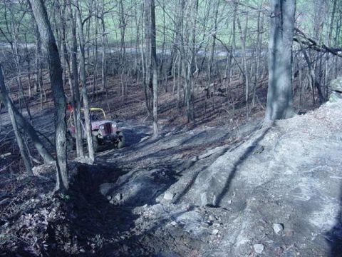 1992 Ford Bronco - A red Jeep navigates a challenging muddy trail through a dense forest.