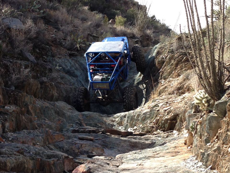 Blue off-road buggy with roll cage climbing a rocky, desert trail