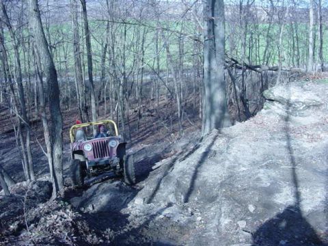 1992 Ford Bronco - A Jeep CJ-7 navigates a challenging off-road trail in a wooded area.