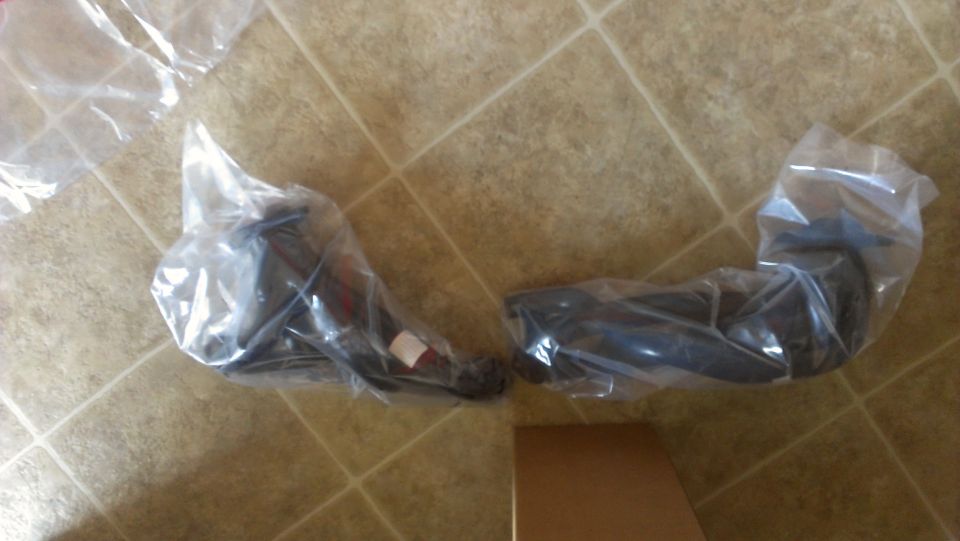 two new suspension parts in plastic wrap on a tiled floor