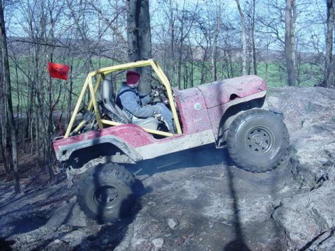 1992 Ford Bronco - A red Jeep Wrangler navigates a challenging off-road course with a driver at the wheel.