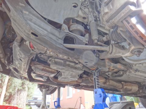 2000 Lincoln Continental - The underside of a car is visible, supported by blue jack stands, with various mechanical parts exposed.