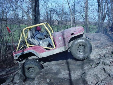 1992 Ford Bronco - This off-road vehicle navigates a challenging muddy incline, its yellow roll cage providing safety.