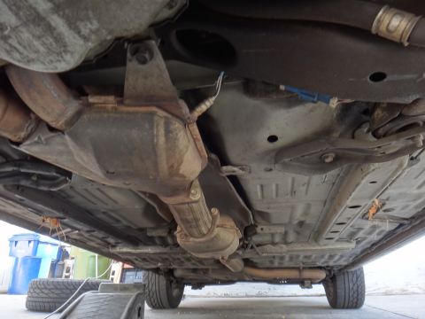 2000 Lincoln Continental - Underside view of a car's exhaust and suspension system, with tires and a trash bin in the background.