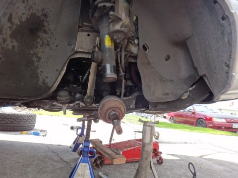 2000 Lincoln Continental - The underside of a vehicle is shown with suspension parts removed for repair, with a red car in the background.