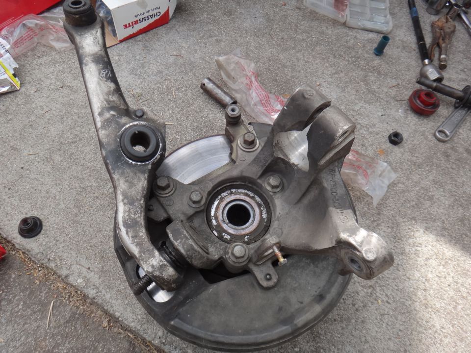 Disassembled suspension knuckle, control arm, and brake rotor on concrete