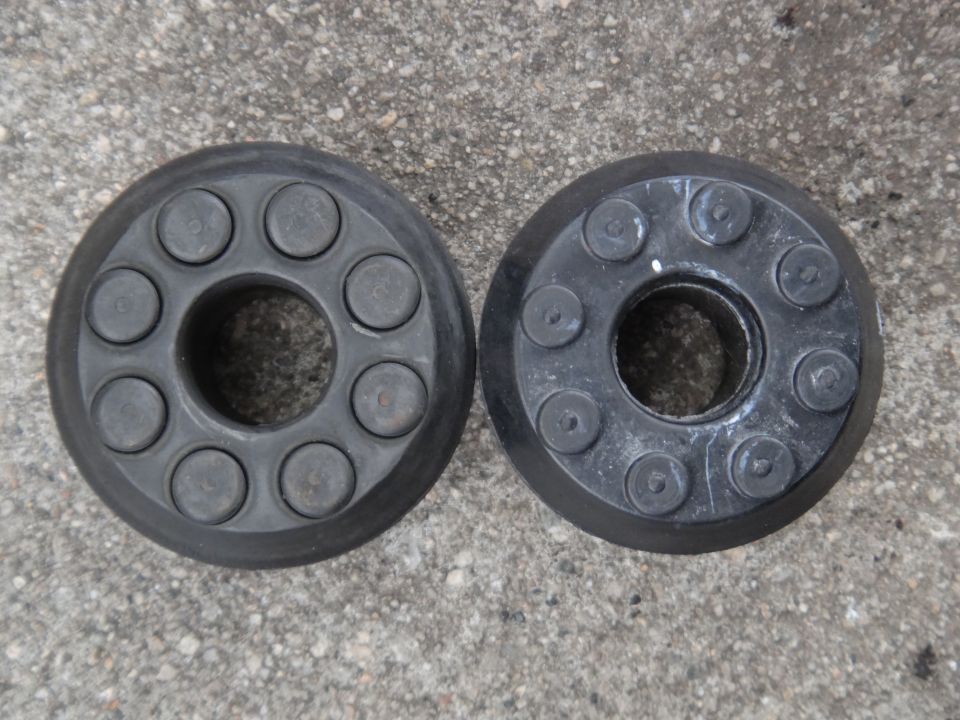 Two black suspension parts with circular metal inserts on a concrete surface