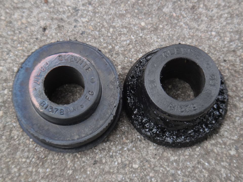 Two rubber suspension bushings on a concrete surface; one is dark gray with pinkish markings, the other is black and degraded