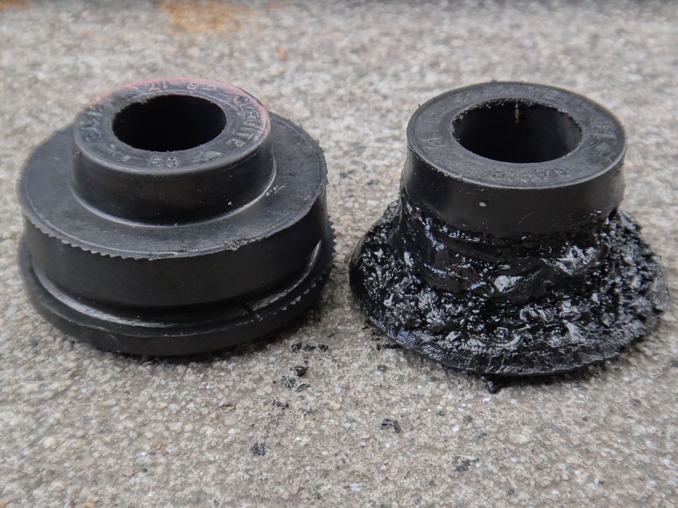Two black rubber suspension bushings on a concrete surface; one is intact, the other is degraded and melted