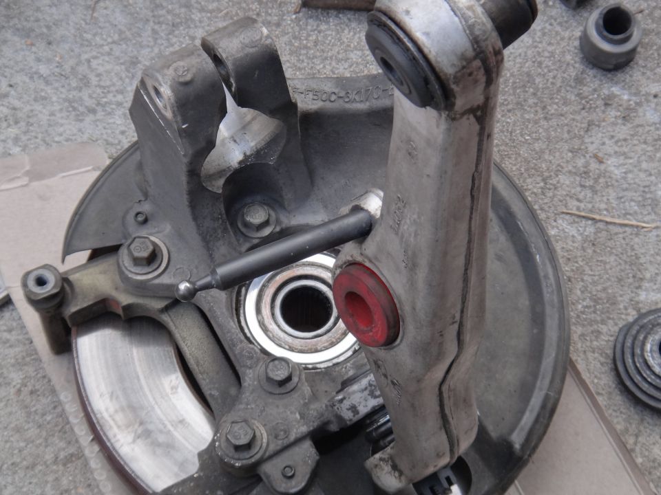 Disassembled car suspension component with brake rotor and bearing visible. Part number F500-5K170-A is stamped on metal