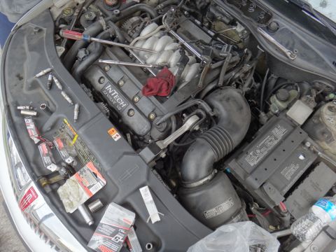 2000 Lincoln Continental - The engine bay of a 2000 Lincoln Continental is shown with various tools and new spark plugs laid out for maintenance.