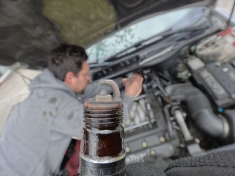 2000 Lincoln Continental - A mechanic is working on a car's engine, with a close-up view of a used spark plug in the foreground.