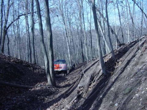 1992 Ford Bronco - A 1992 Ford Bronco navigates a wooded trail, its red body contrasting with the bare trees.