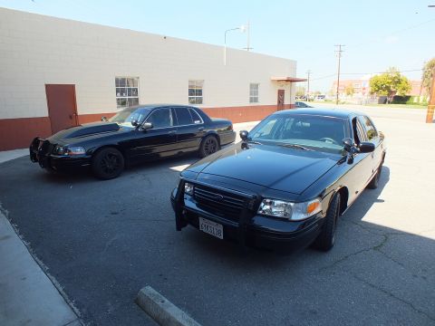 2003 Ford Crown Victoria - Pair of blacked-out Ford Crown Victoria Police Interceptor sedans with brush guards in a parking lot