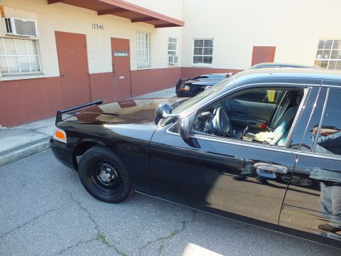 2003 Ford Crown Victoria - Low front-quarter shot of a black Crown Victoria with steel wheel beside a Custom Mfg Co building.