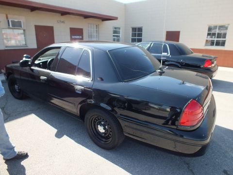 2003 Ford Crown Victoria - Two black Crown Victoria sedans parked rear-angled outside a tan industrial unit numbered 12946.