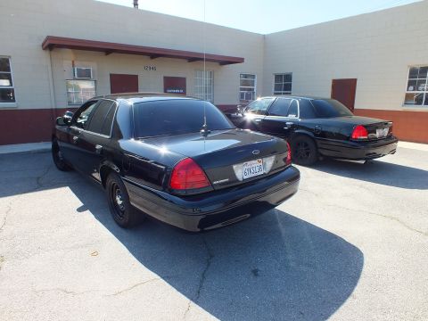 2003 Ford Crown Victoria - Rear of a black Crown Victoria Police Interceptor, plate 6YKS138, parked near a second black sedan.