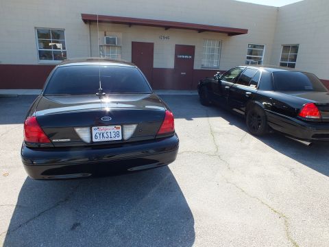 2003 Ford Crown Victoria - Tail-on view of a black Crown Victoria with California plate 6YKS138 and a matching car alongside.