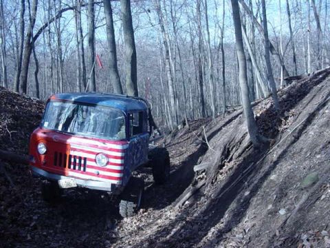 1992 Ford Bronco - An off-road vehicle with a custom paint job navigates a steep, wooded incline.