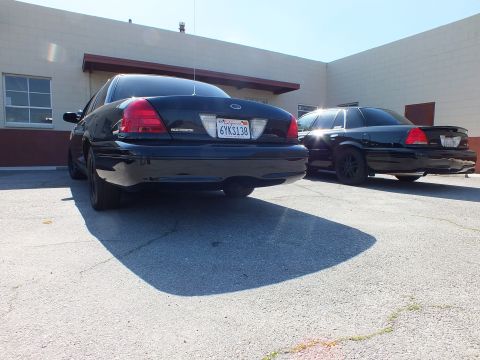 2003 Ford Crown Victoria - Low rear shot of a Crown Victoria Police Interceptor, plate 6YKS138, with a black twin nearby.