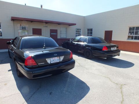 2003 Ford Crown Victoria - Black Crown Victoria 6YKS138 and a matching sedan parked at angles outside an industrial building.