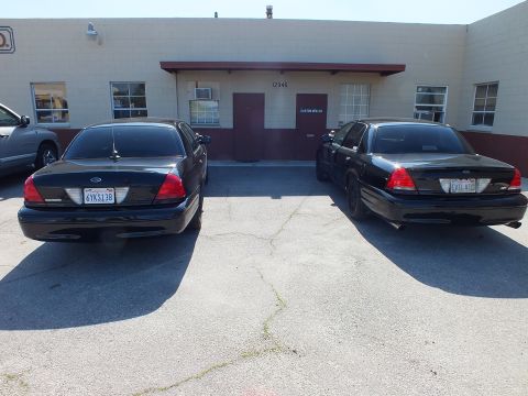 2003 Ford Crown Victoria - Rear view of two black Crown Victoria sedans, one tagged 6YKS138 and the other EVIL VIC.