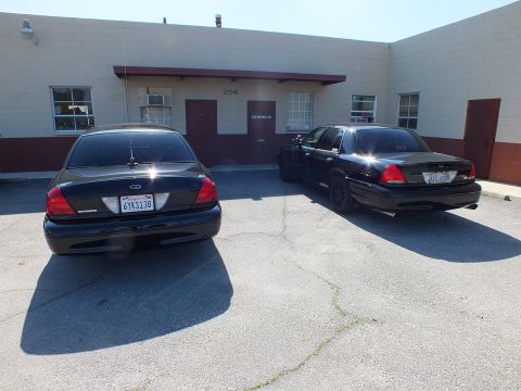 2003 Ford Crown Victoria - glossy black Crown Victoria, plate 6YKS138, parked beside a darker matte sedan at the lot.