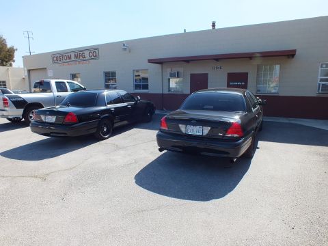 2003 Ford Crown Victoria - Black Crown Victoria EVIL VIC parks near a second sedan and a white pickup at Custom Mfg Co.