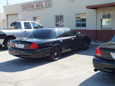2003 Ford Crown Victoria - Black Crown Victoria on steel wheels sits before the Custom Mfg Co sign with a white pickup behind.