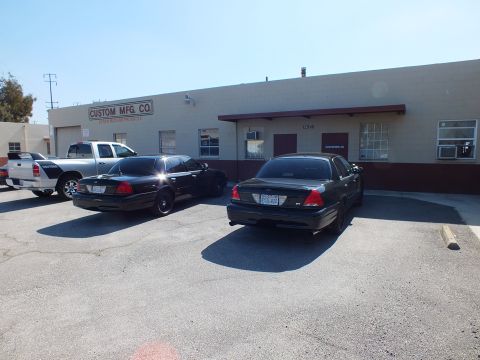 2003 Ford Crown Victoria - Two black Crown Victoria sedans and a white pickup parked outside the Custom Mfg Co building.