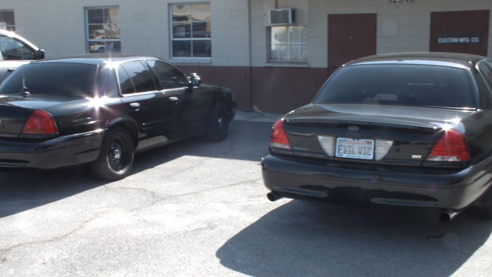 Two black Ford Crown Victoria sedans rear view, one plated EVIL VIC, by Custom Mfg Co