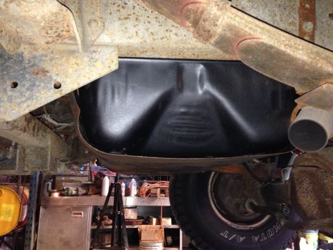 1979 Ford Bronco - The underside of a vehicle shows a black fuel tank and part of the exhaust system, with a workshop visible below.