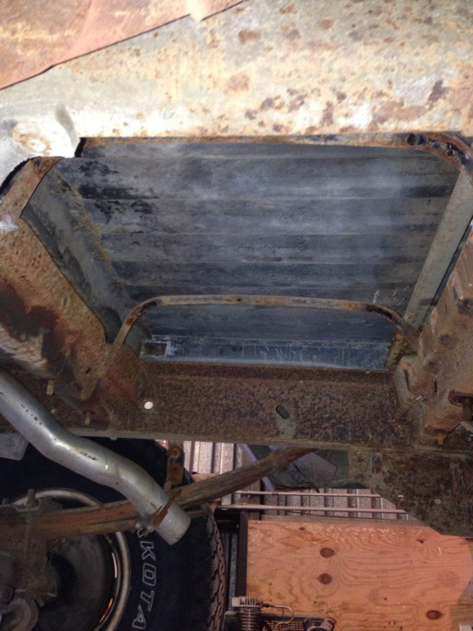 Undercarriage of a rusty vehicle with leaf springs and exhaust pipe visible
