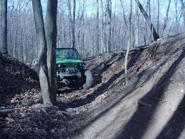 Green off-road SUV with aftermarket bumper and winch on a wooded dirt trail
