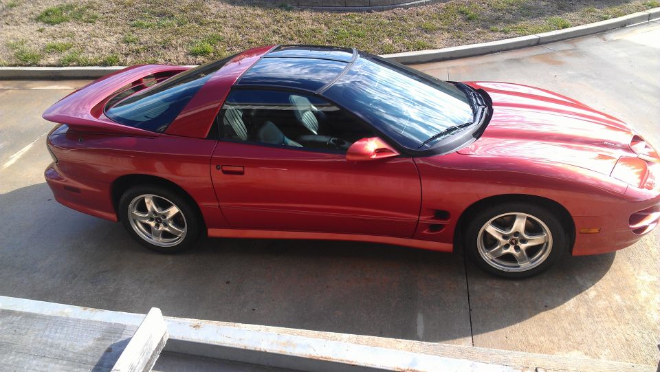 Red coupe with black t-top roof, side view. Looks like a late 90s Pontiac Firebird