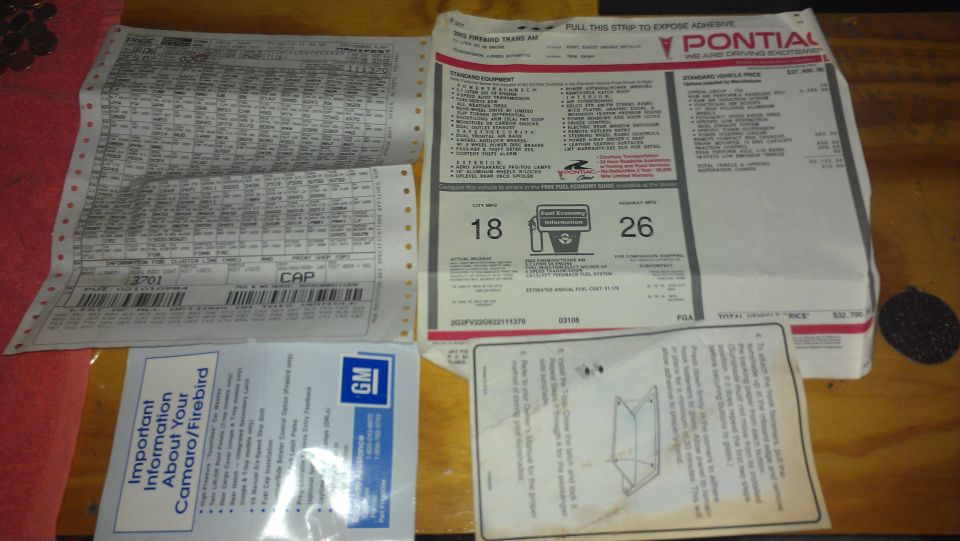 Several car documents, including a window sticker and build sheet, are spread out on a wooden surface