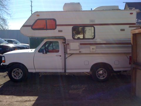 1986 Yugo GV - Side view of a white pickup truck fitted with a white camper shell, orange windows and brown trim.
