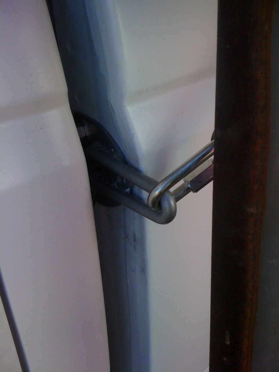 Welded steel tie-down loop with hook in the gap between white pickup bed and camper