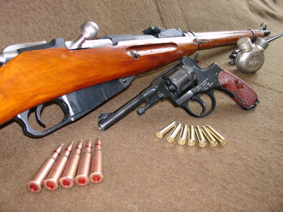 Rifle, revolver, and ammunition laid out on a brown textured surface