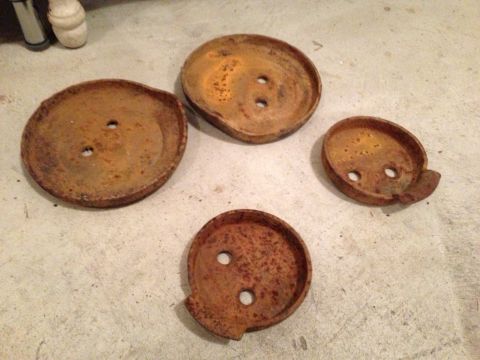 1989 Ford Bronco - Four rusty metal caps with two holes each are scattered on a concrete surface.